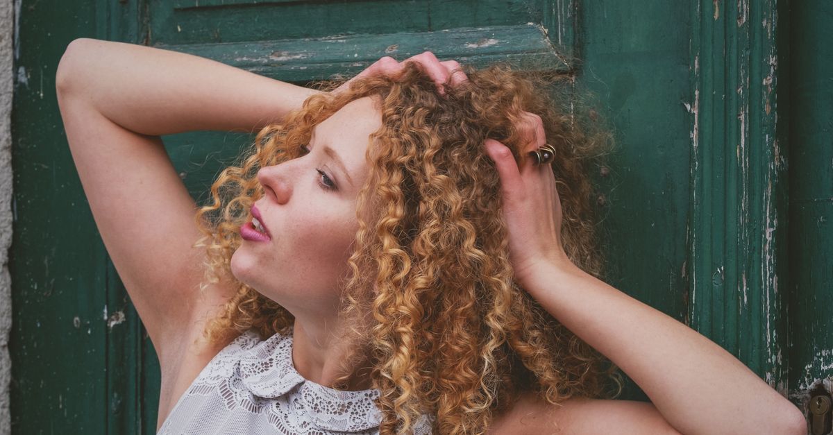 Femme aux cheveux bouclés texturés observant sa chevelure en lumière naturelle